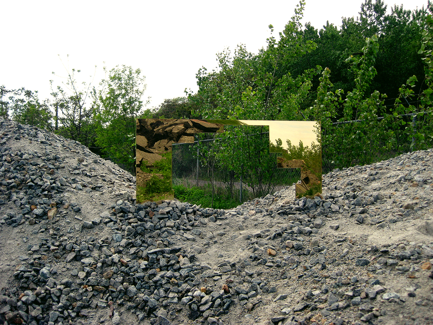 Gold reflective mirror of negative space around a building shape outdoors in a gravel pile