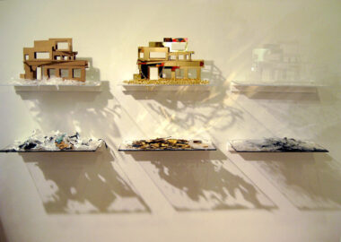 Sculpture wall installation of six shelves with three abstract modern houses in different materials displayed on them