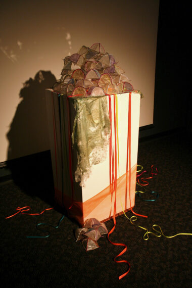 Spotlit sculpture of tent shapes on a plinth with trailing ribbons